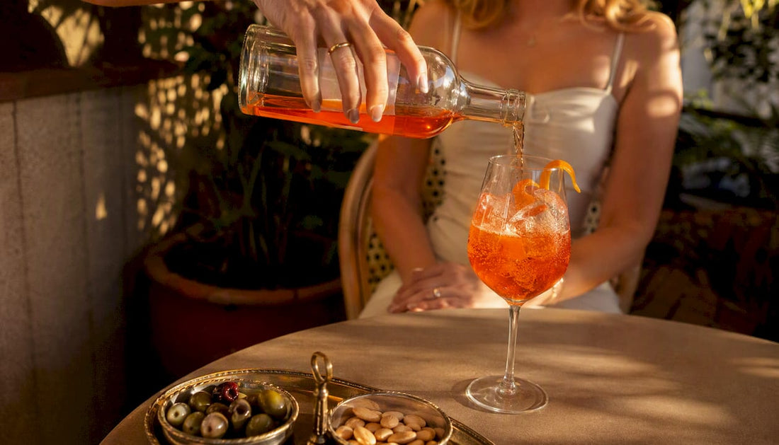 Hand pouring Aperol Spritz with olives and nuts